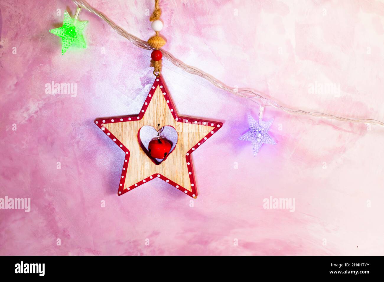 Holzstern mit Glocke und Perlen und Weihnachtsbaumgirlande. Weihnachtsschmuck. Karte. Speicherplatz kopieren. Stockfoto
