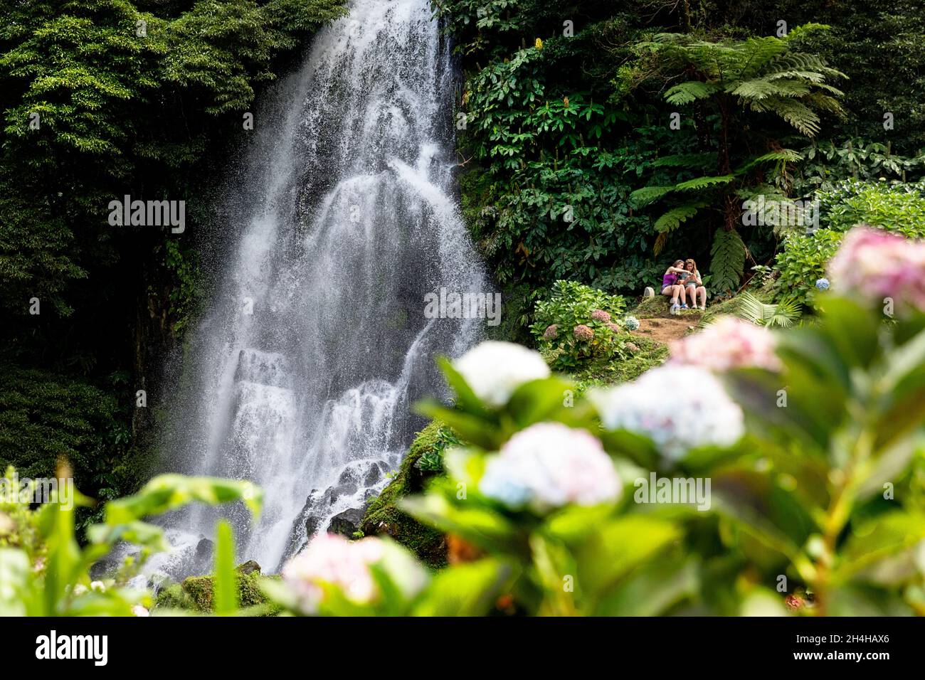 Touristen sitzen auf einer Bank in der Nähe des Ribeira dos Caldeirões Wasserfalls auf der Insel Sao Miguel, Azoren, Portugal Stockfoto