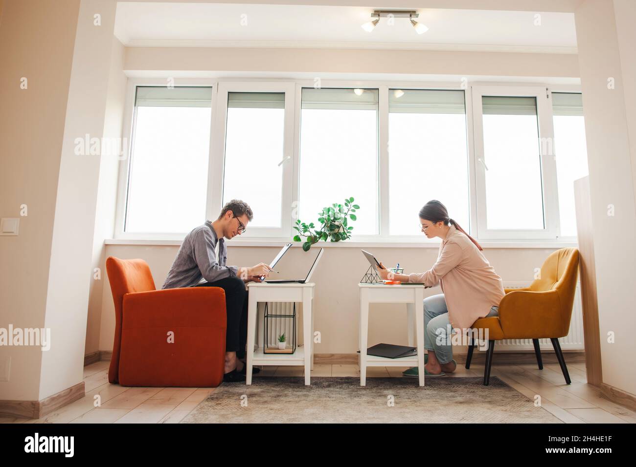 Seitenansicht eines Paares, das aufgrund einer Pandemie von zu Hause aus arbeitet. Stehen auf der Couch vor einander. Arbeiten aus der Ferne. Stockfoto