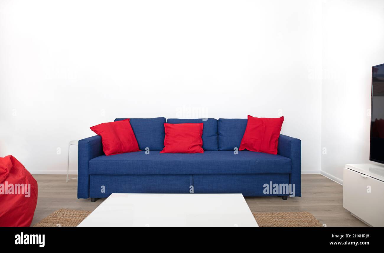 Blaues Sofa mit roten Kissen vor weißer Wand Stockfoto