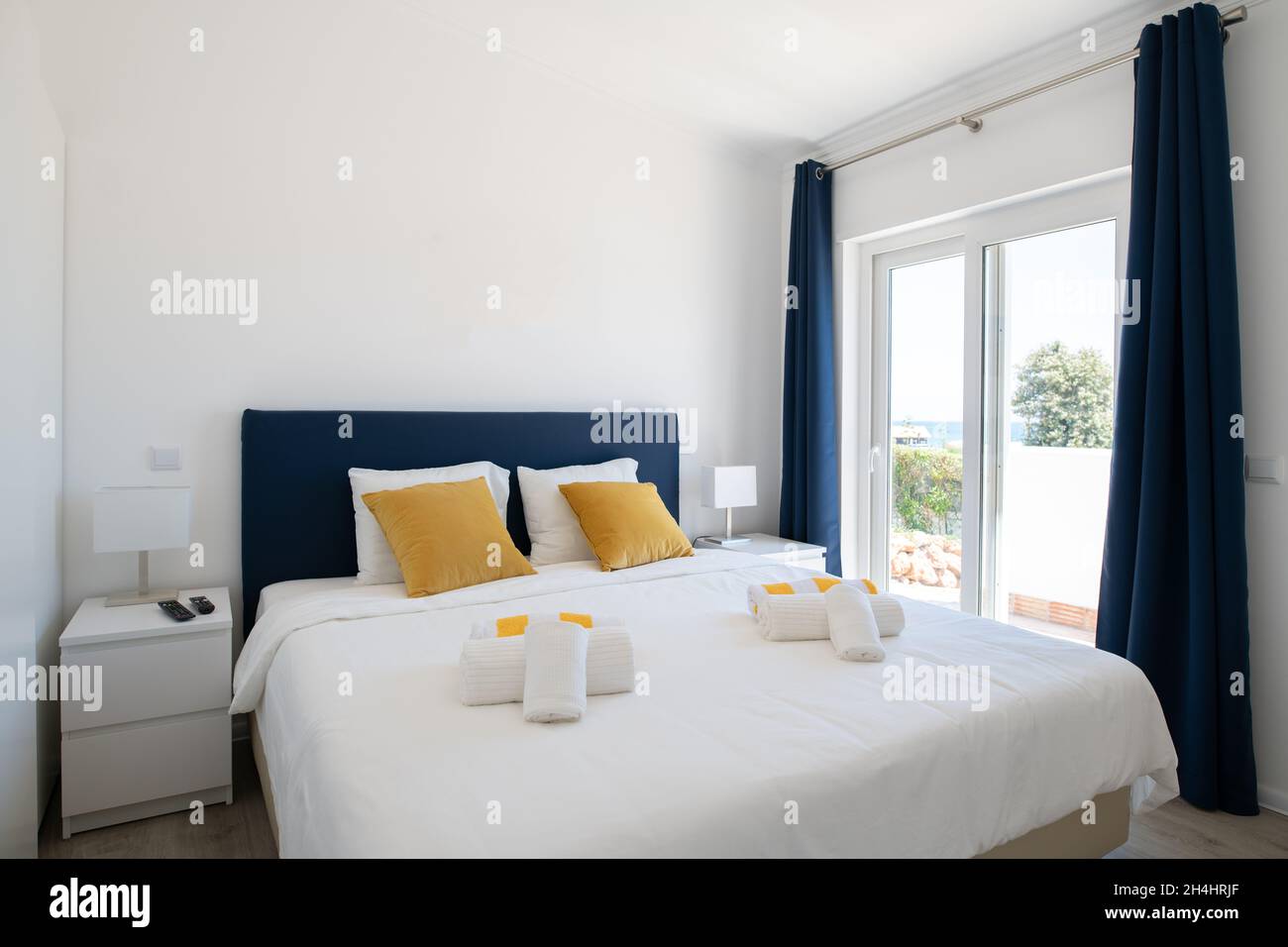 Doppelzimmer mit weißer Bettwäsche, blauem Kopfteil und Glasschiebetüren zur Terrasse Stockfoto