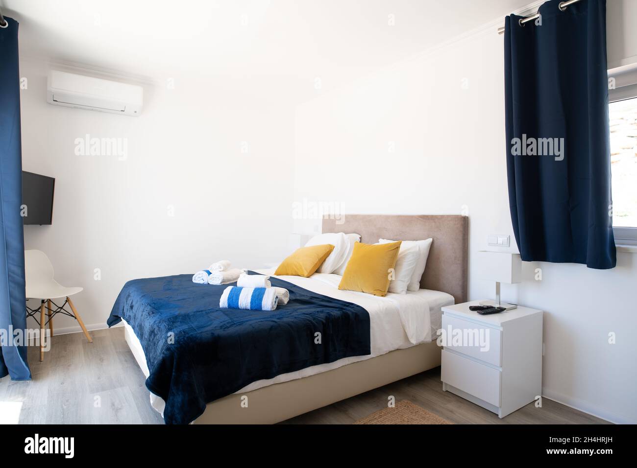 Doppelbett mit blauem Überwurf, gelben Kissen und weißem Bettbezug Stockfoto