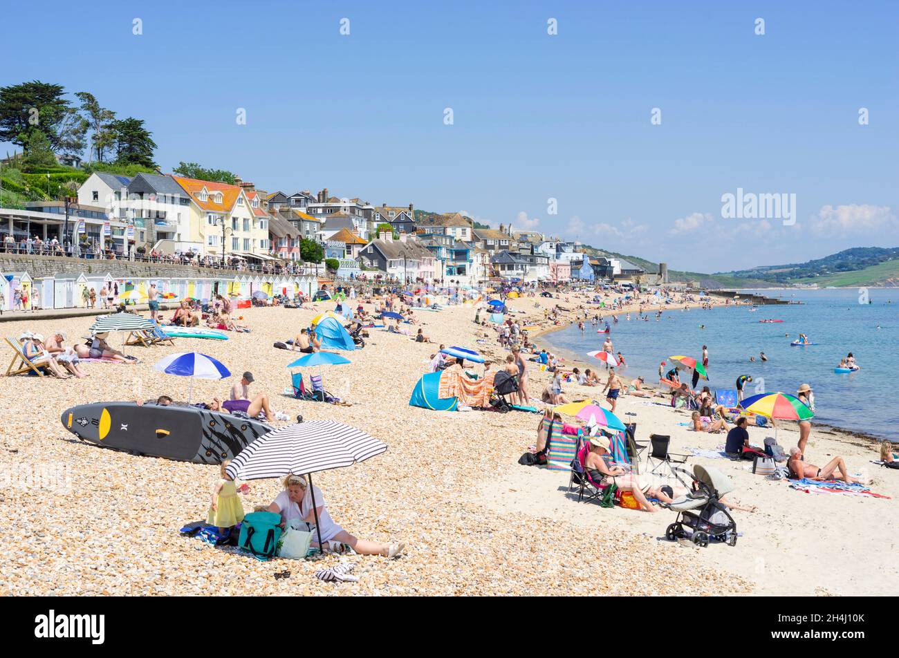 Familien am Strand mit Pop-up-Strandzelten Liegestühle Sonnenschirme und Paddle-Boards am Sandstrand bei Lyme Regis Dorset England GB Europa Stockfoto