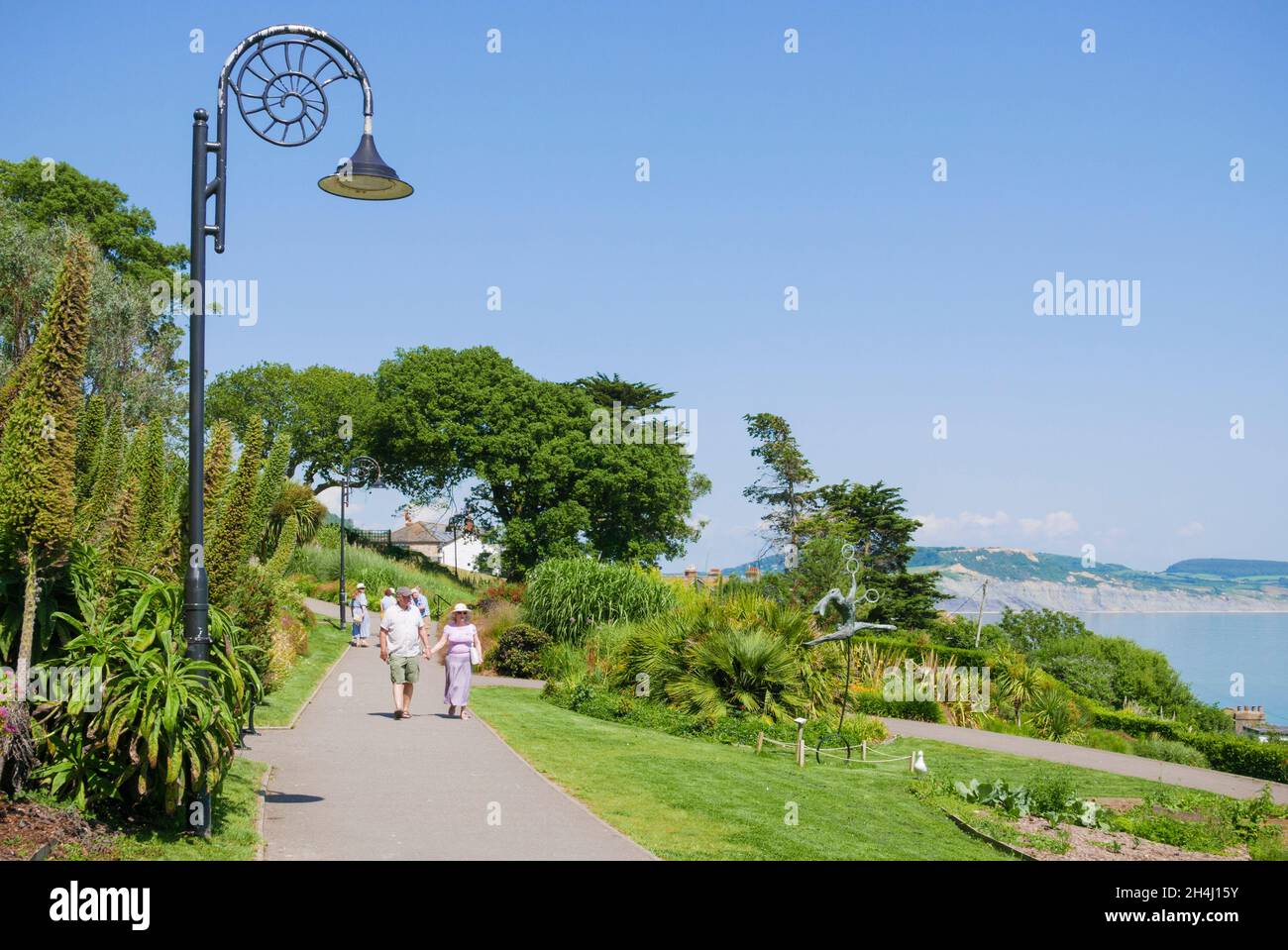 Lyme Regis Ammonit inspirierte Lampenpfosten und Menschen zu Fuß in den Gärten Langmoor und Lister Lyme Regis Dorset England GB Europa Stockfoto