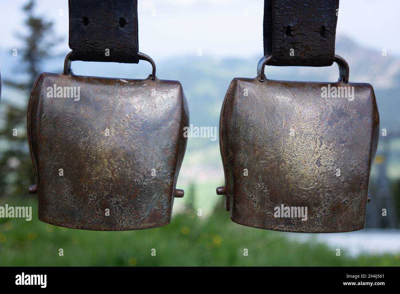 Zwei große messingfarbene Kuhglocken wurden aufgehängt. Im Hintergrund sieht man eine Berglandschaft Stockfoto