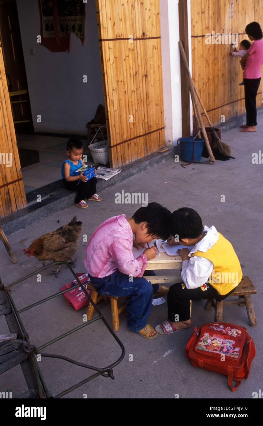 China 2000er Jahre. Chinesische Kleinkinder arbeiten an einem Tisch und Stühlen in Kindergröße im Innenhof ihres Familienbaums. Ein Huhn wandert vorbei, ihr Bruder sitzt vor der Türschwelle. Yiwu, Provinz Zhejiang 2001. HOMER SYKES Stockfoto