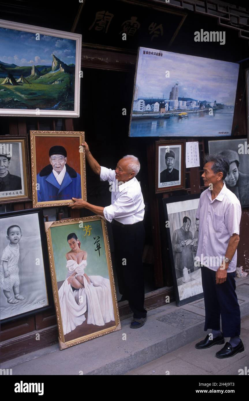 Lanxi, Provinz Zhejiang, China, 2001, 2000er Jahre. Ein lokaler Künstler zeigt seine Ölgemälde neben seinem Laden, ein männlicher Passant mittleren Alters kommt an Stops vorbei, um sie zu bewundern. HOMER SYKES Stockfoto