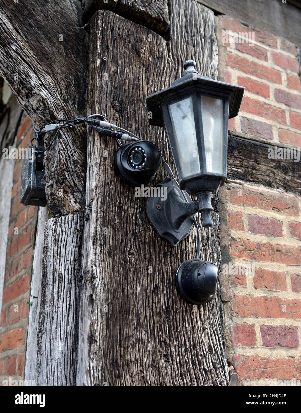 Zwei Sicherheitskameras für den Außenbereich und eine Wandleuchte auf einem Holzrahmen aus altem, traditionellem Gebäude in Großbritannien Stockfoto