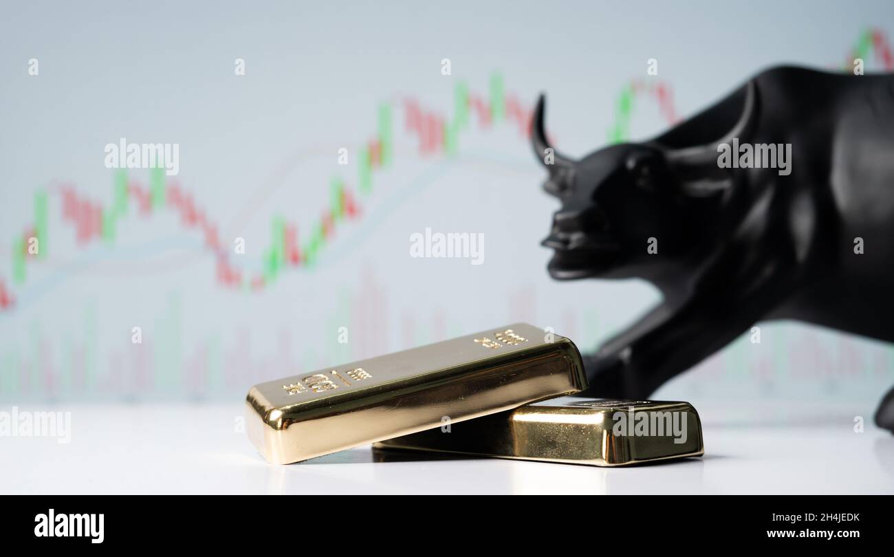 Konzentrieren Sie sich auf Goldbarren, das Konzept der bullischen oder boomenden Goldmarktaktien oder Aktien, die nach Bullen hinter den Goldbarren mit Charts im Hintergrund angezeigt werden. Stockfoto