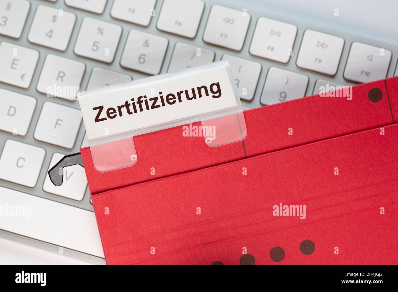 Das deutsche Wort für Zertifizierung ist auf dem Etikett einer roten Hängemappe zu sehen. Der Hängeordner befindet sich auf einer Computertastatur. Stockfoto