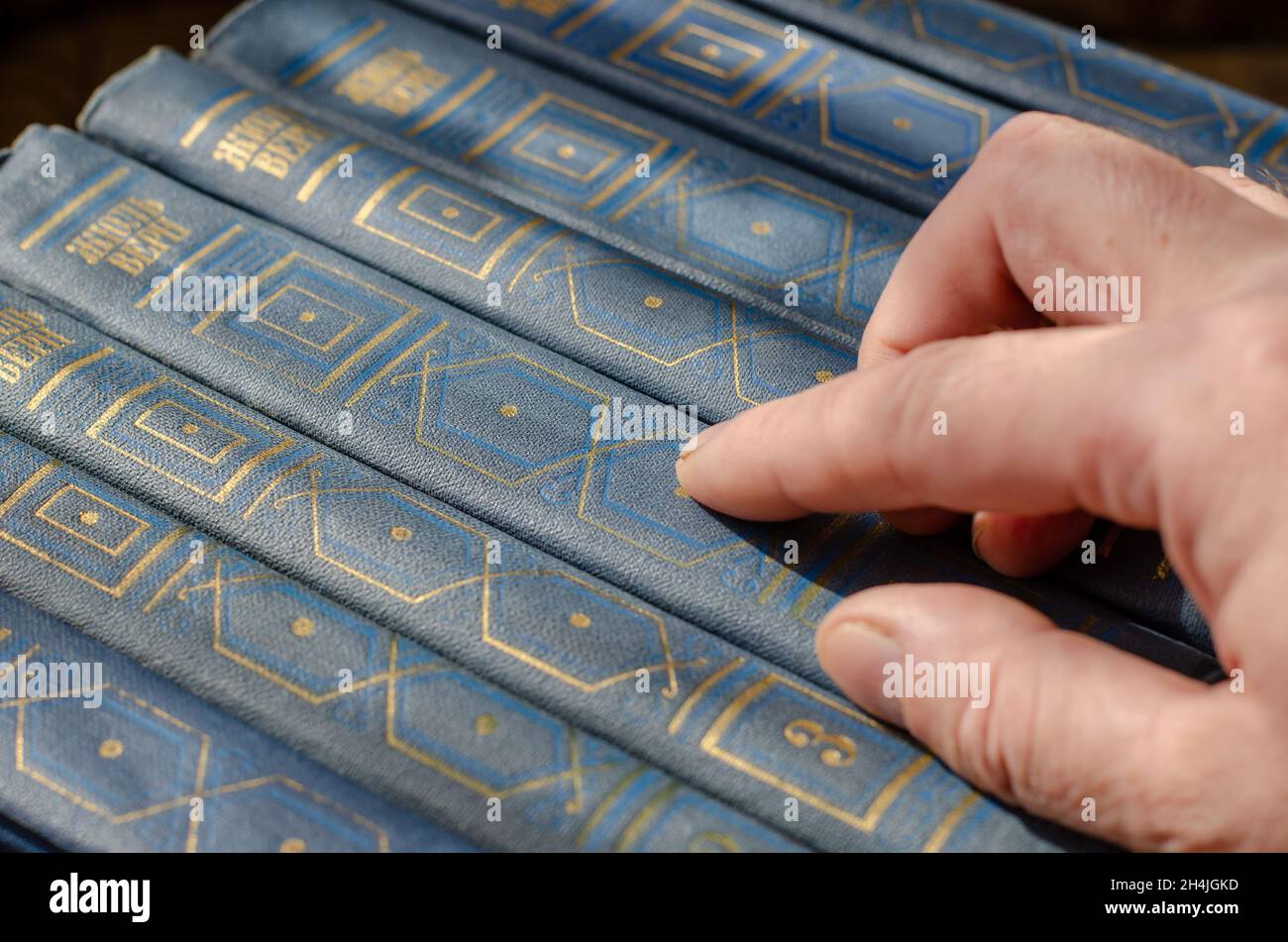 Der Mann zeigt mit dem Zeigefinger auf die Romane von Jules Verne. Blaue Hardcover-Bücher mit literarischen Werken des berühmten französischen Schriftstellers. Multivolume c Stockfoto