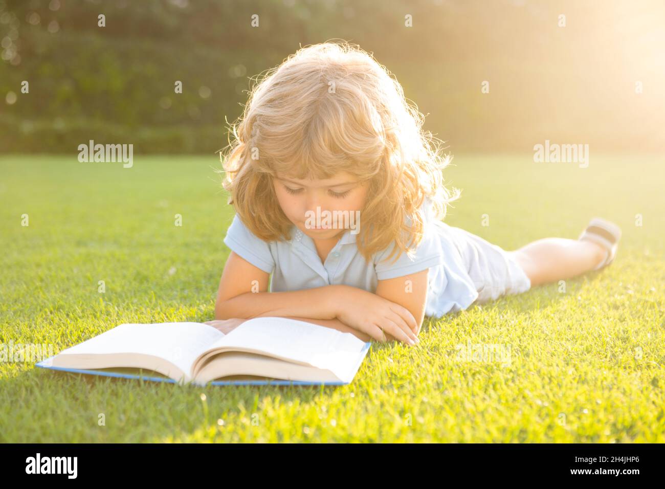 Intelligente Kinder. Kleiner Junge, der im Sommer bei Sonnenuntergang ein Buch liest. Sommer Outdoor Kindererziehung Stockfoto