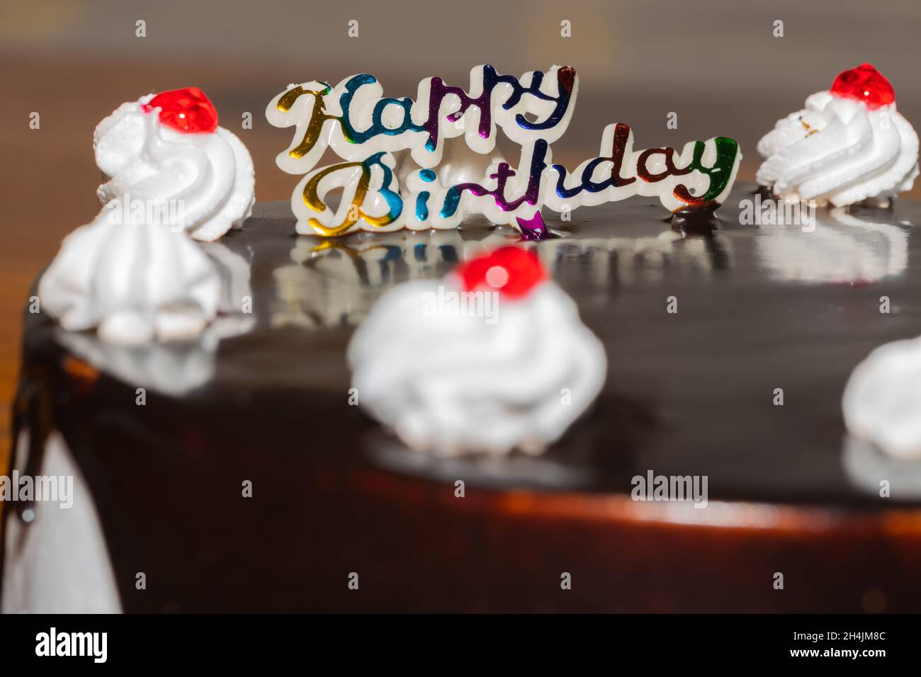 Nahaufnahme eines Schokoladenkuchens mit frischer weißer Creme und Kirsche Belag und Happy Birthday darauf geschrieben Stockfoto