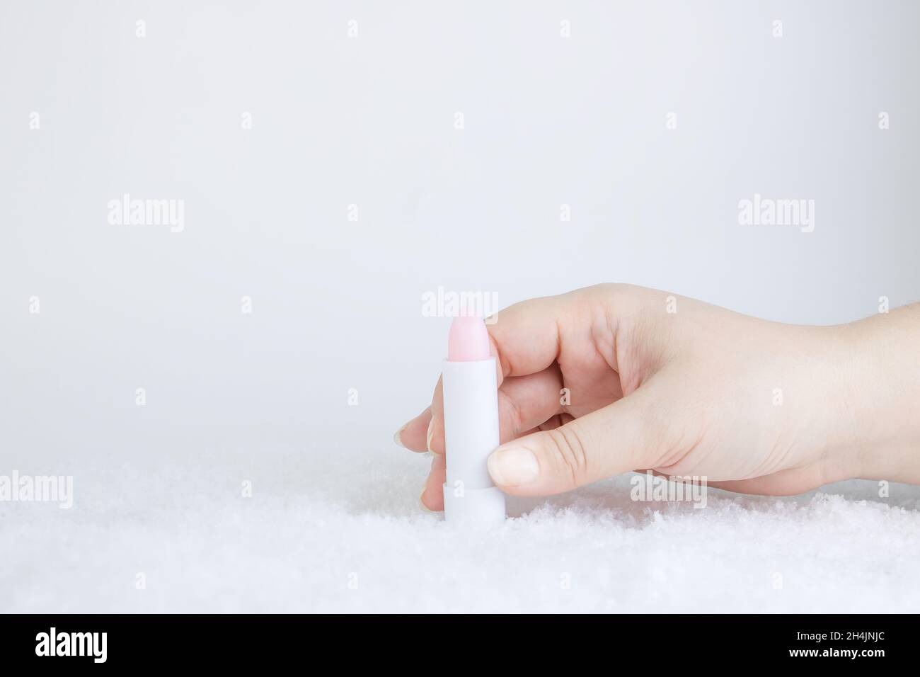 Eine weiße Tube rosa Lippenstift-Balsam zum Schutz und zur Pflege der Lippen. Kosmetik für die Wintersaison. Behälter in der Hand einer Frau im Schnee nachmachen. Weihnachten PR Stockfoto