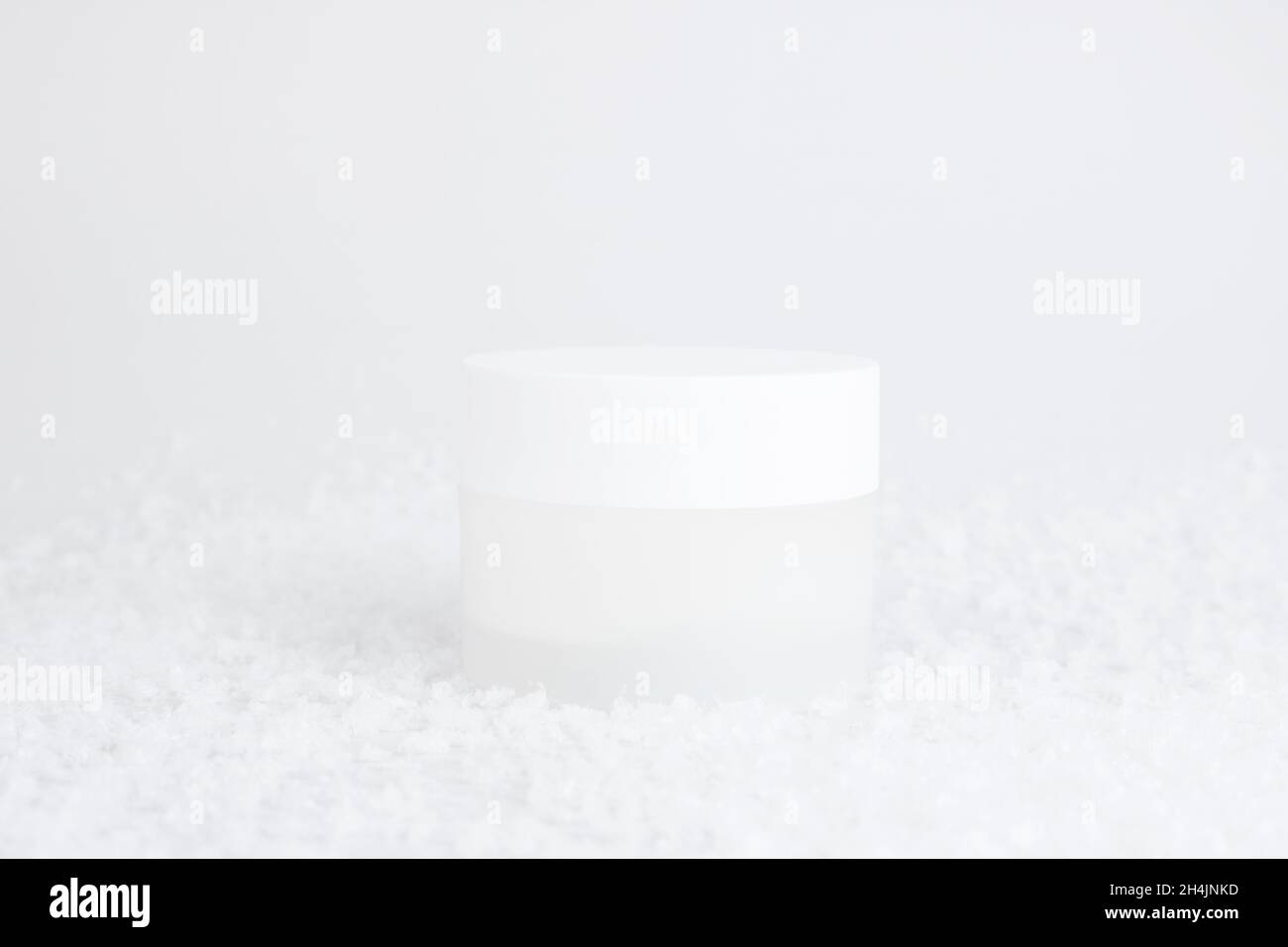 Glas kosmetische Creme auf weißem Hintergrund mit Schnee. Behälter für Körperpflegebalsam. Kosmetik für die Wintersaison. Behälter im Schnee nachmachen. Weihnachten Stockfoto