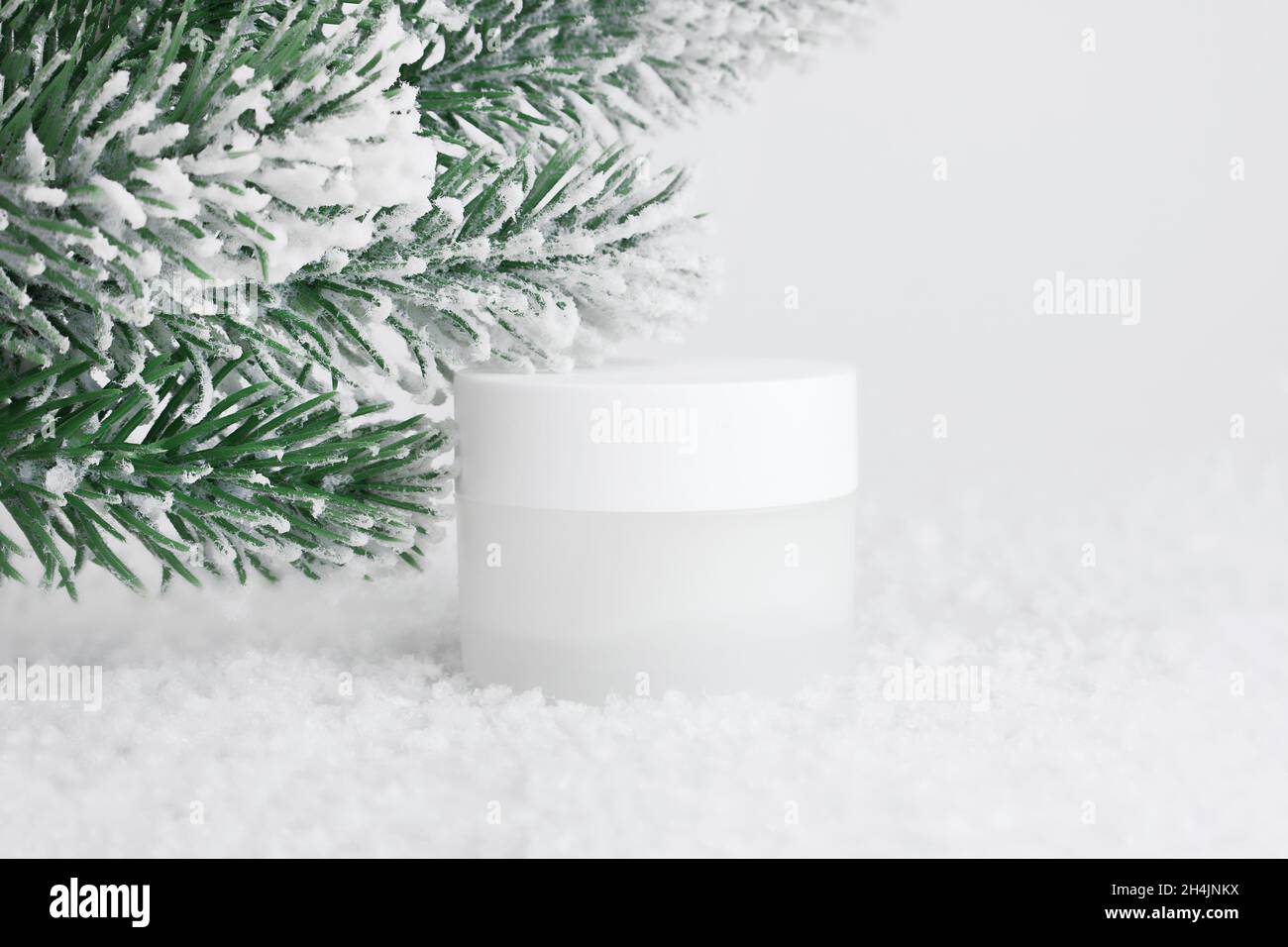 Glas kosmetische Creme auf weißem Hintergrund mit Schnee. Behälter für Körperpflegebalsam. Kosmetik für die Wintersaison. Behälter im Schnee nachmachen. Weihnachten Stockfoto