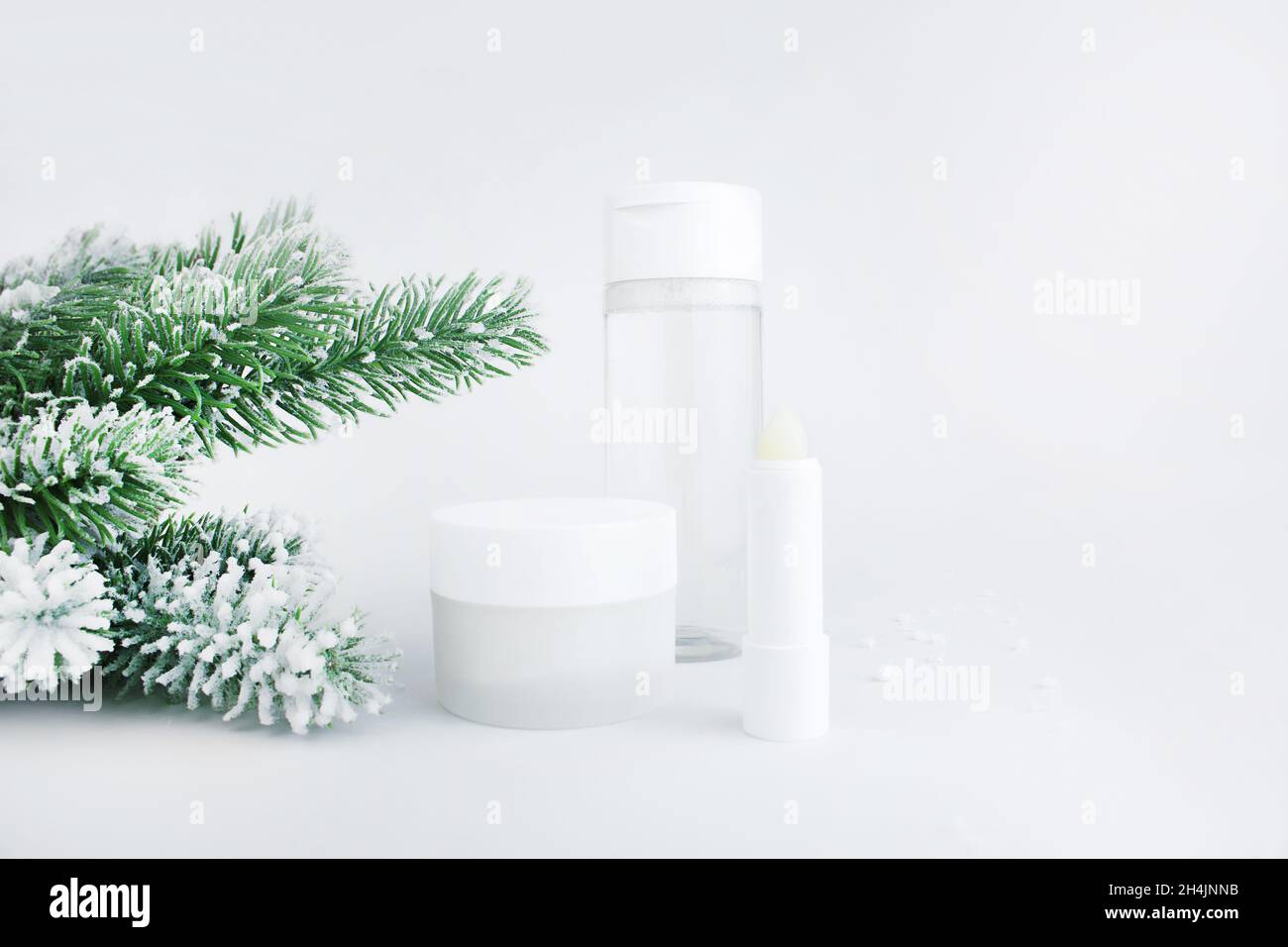 Hautpflegeflaschen auf schneebedeckter Oberfläche. Kosmetik für die Wintersaison. Leere Behälter mit Tannenzweigen im Hintergrund. Weihnachtsgeschenk für Frauen ide Stockfoto