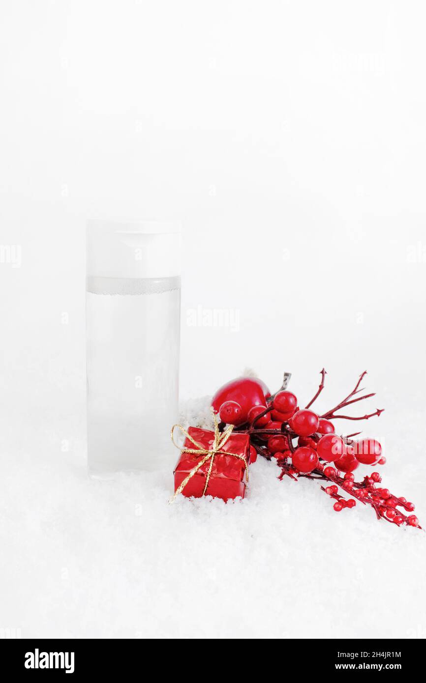 Hautpflegeprodukt auf dem Schnee, mit Weihnachtsdekorationen.Gesichtsreiniger oder mizellare Wasserflasche Mockup mit dekorativen Zweigen eines Weihnachtsbaums. Stockfoto