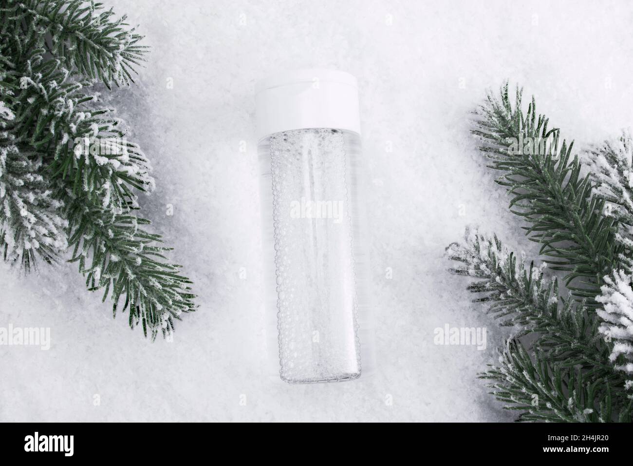 Hautpflegeprodukt flach auf Schneehintergrund legen. Gesichtsreiniger oder mizellare Wasserflasche Mockup mit dekorativen Zweigen eines Weihnachtsbaums, firbackdro Stockfoto