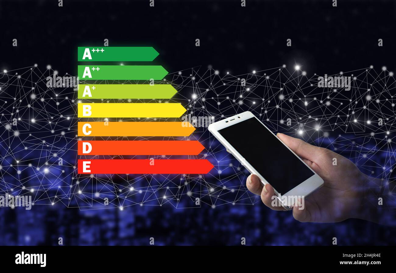 Energieeffizienzkonzept. Handgriff weißes Smartphone mit digitalem Hologramm Energieeffizienz-Zeichen auf Stadt dunkel verschwommen Hintergrund Stockfoto