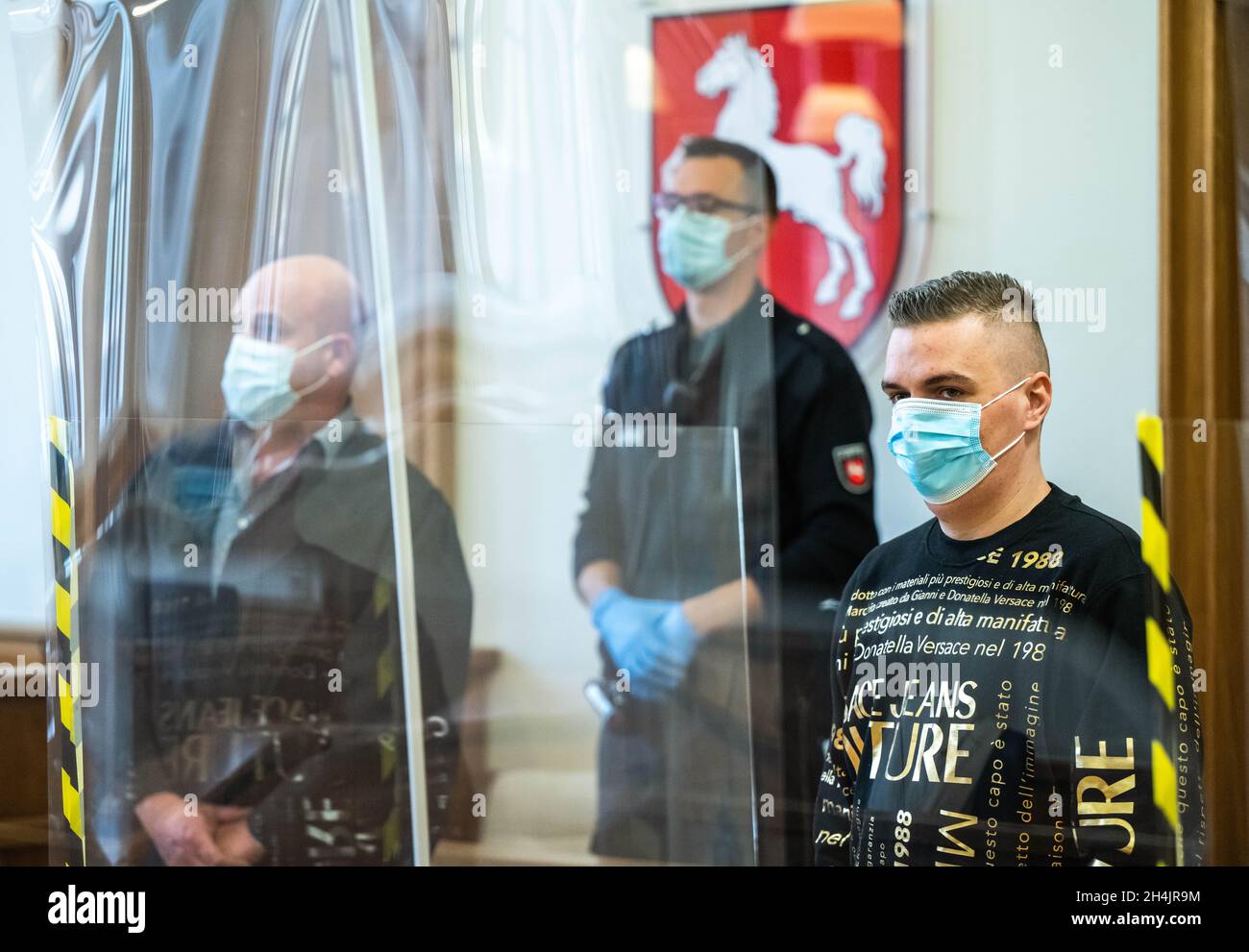 Oldenburg, Deutschland. November 2021. Der Angeklagte (r) steht zu Beginn des Prozesses im Gerichtssaal des Landgerichts. Er soll gefälschte Goldbarren und Krügerrand-Münzen über eine Online-Plattform verkauft haben. Dabei soll er Schäden von rund 40,000 Euro verursacht haben. Kredit: Mohssen Assanimoghaddam/dpa/Alamy Live Nachrichten Stockfoto