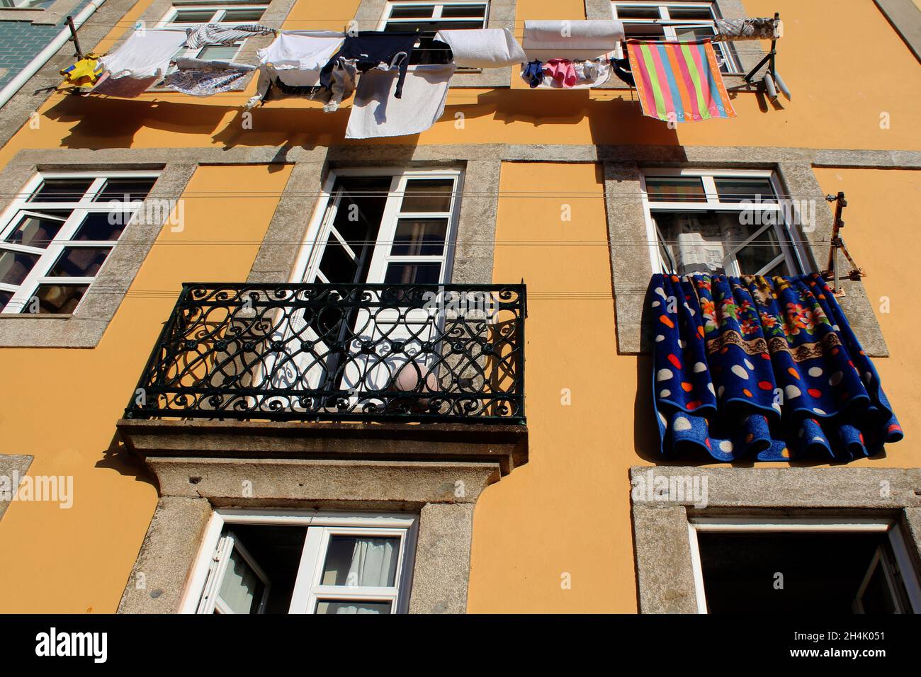 Bunte Wäsche trocknet in der Sonne an einer Wäscheleine, die an einer gelben Hauswand gebracht ist in Porto, Portugal. Stockfoto