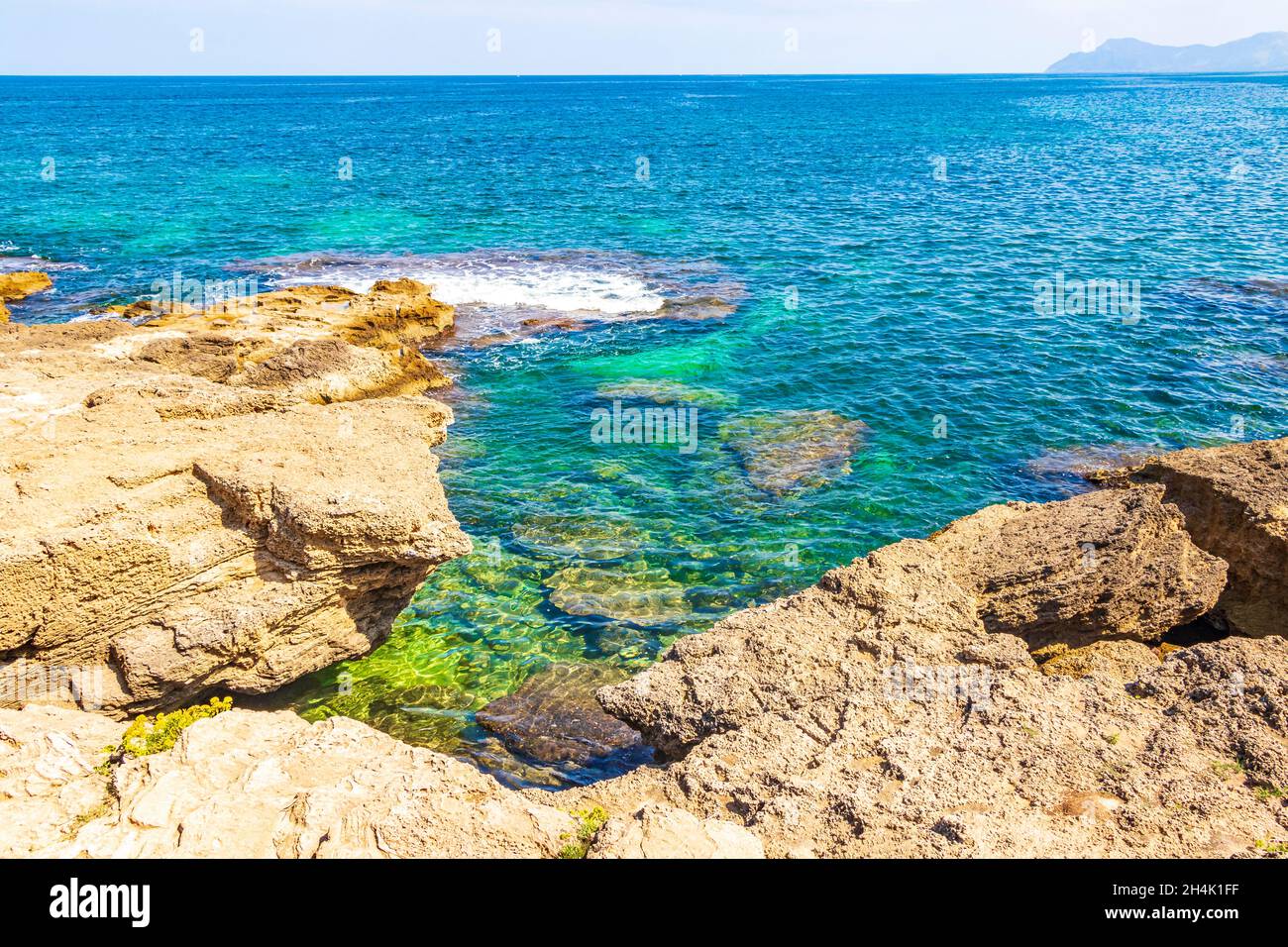 Raue natürliche Küsten- und Strandlandschaft Panorama mit türkisfarbenen Wellen Berge Felsen Felsbrocken und Steine in Can Picafort auf der Baleareninsel M Stockfoto