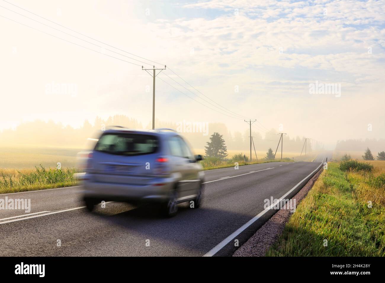 Auto fährt mit Geschwindigkeit auf der Landstraße an einem schönen nebligen späteren Sommermorgen. Bewegungsunschärfe in der Kamera. Stockfoto