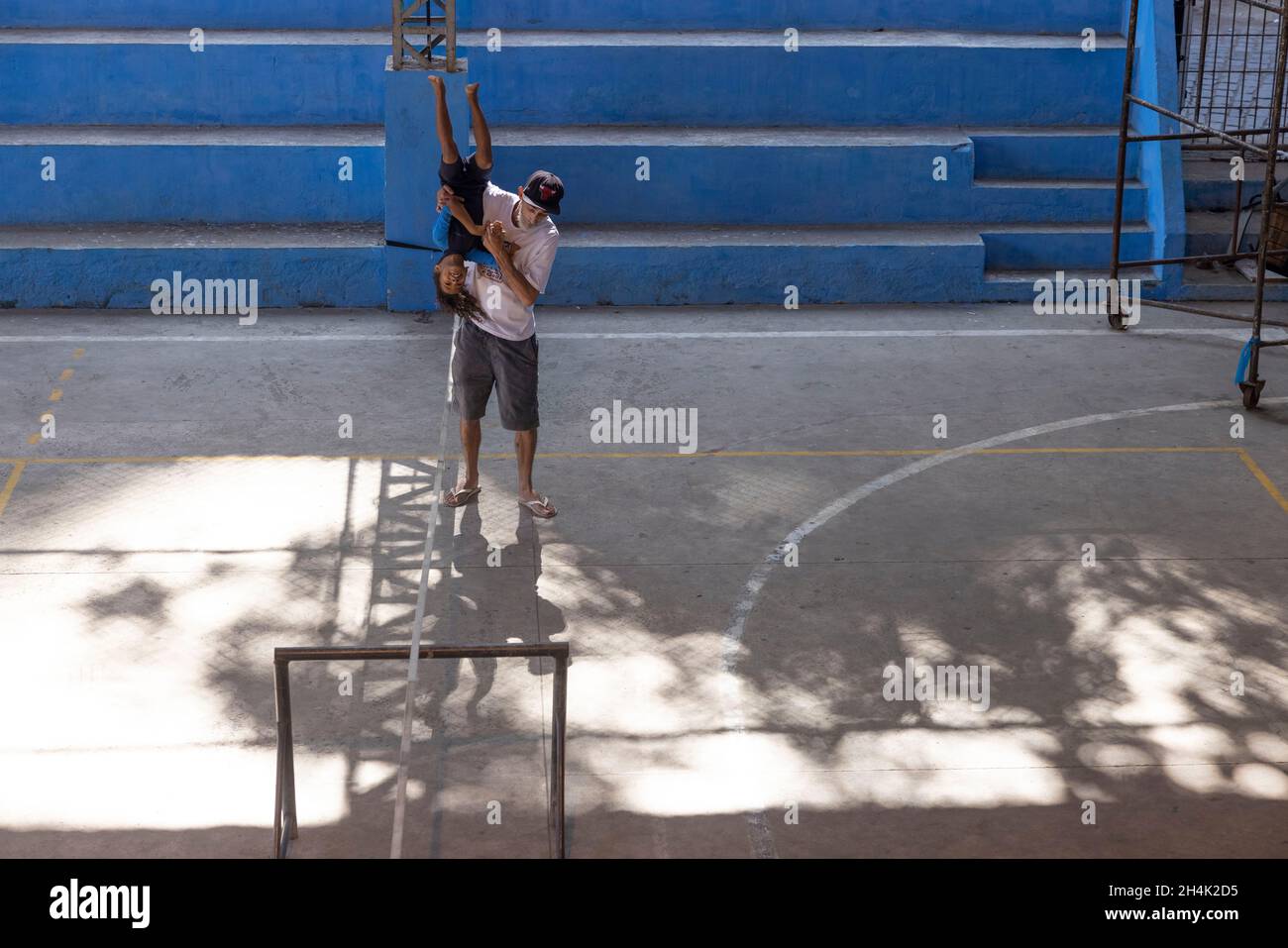 Brasilien, Rio de Janeiro, Favela Babilonia, auf Initiative des Maewan-Vereins und der lokalen Verbände Favelasonha und Mawon während einer Kooperation zur Förderung des Sports in den Favelas, den beiden Highlinern Antony Newton und Pablo Signoret, mehreren Highline-Weltmeistern, Eine Initiation Slackline in der Favela-Turnhalle installiert haben, unternimmt Eloise, 8 Jahre alt, noch in einem Neoprenanzug, ihre ersten Schritte auf der Slackline mit Valdemir, Das Gymnasium ist der privilegierte Ort des Lebens für diese Kinder, die aufgrund der COVID-Krise seit 2 Jahren nicht mehr zur Schule gehen konnten Stockfoto