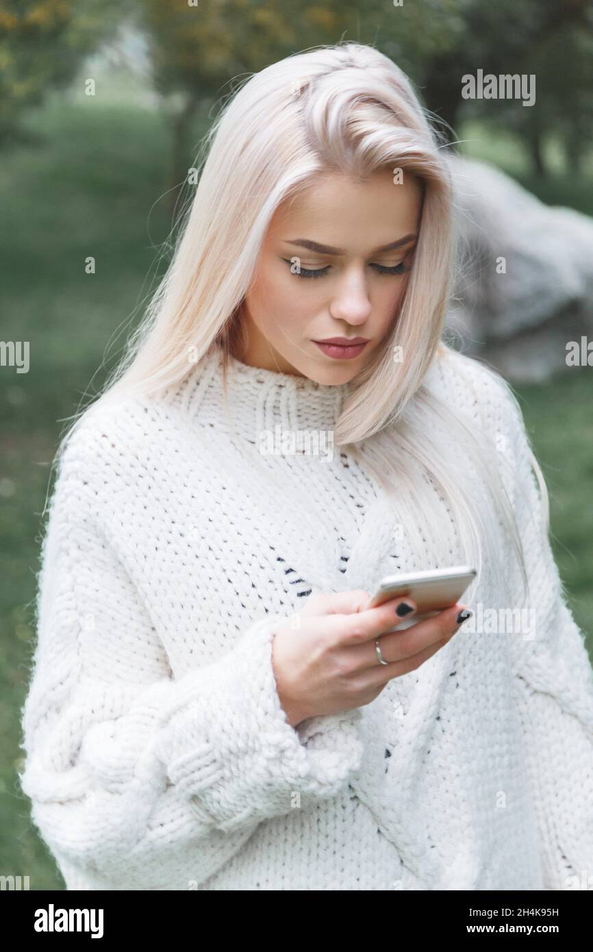 Portrait der jungen kaukasischen blonden Haare Frau in weißen Pullover nutzt das Telefon im Freien. Stockfoto