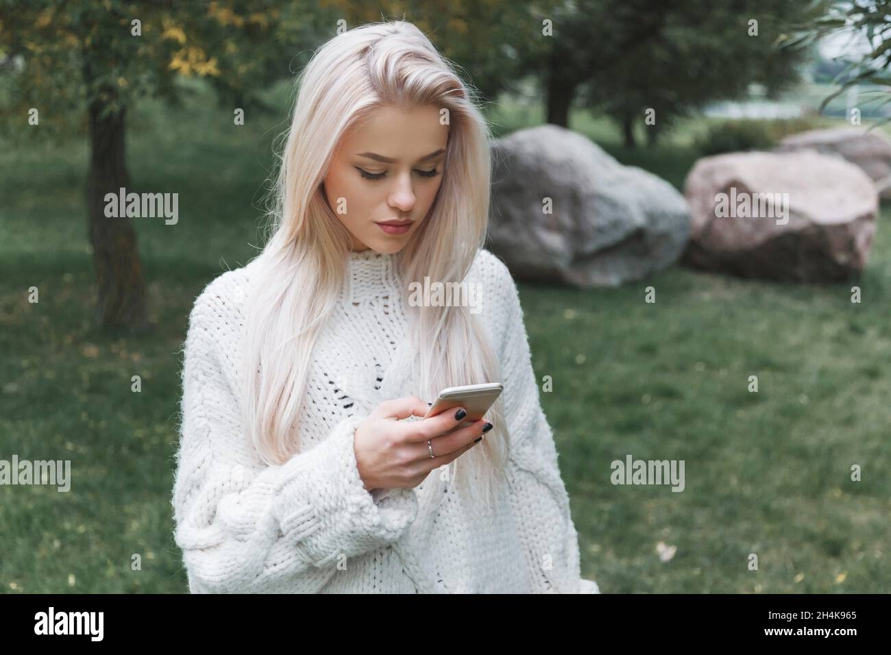Junge kaukasische blonde Haare Frau in weißen Pullover nutzt das Telefon im Freien. Stockfoto