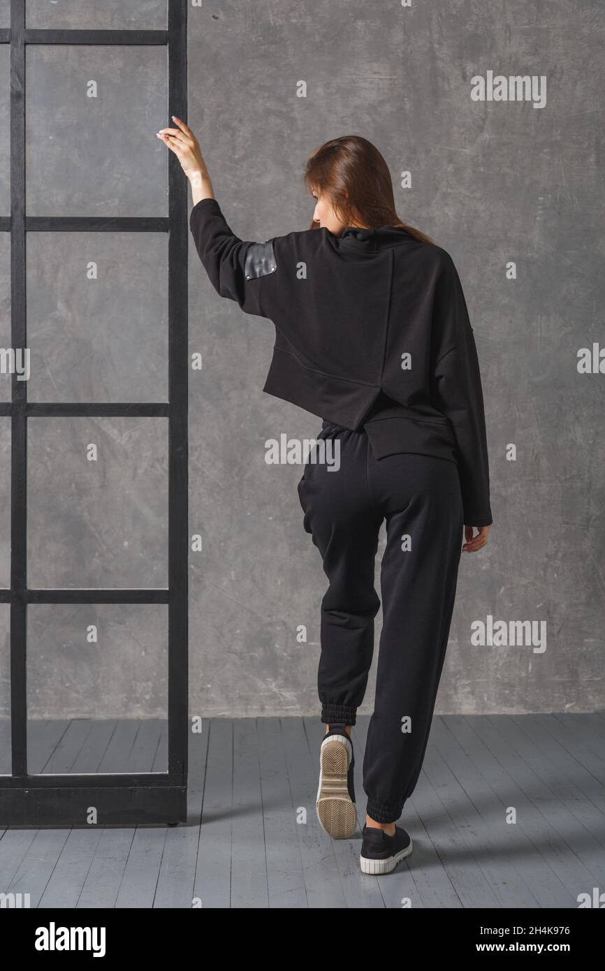 Junge Frau in schwarzer Sportkleidung, Hose und Sweatshirt. Rückansicht. Konzept der modischen Sport-Outfit, drinnen Foto. Stockfoto