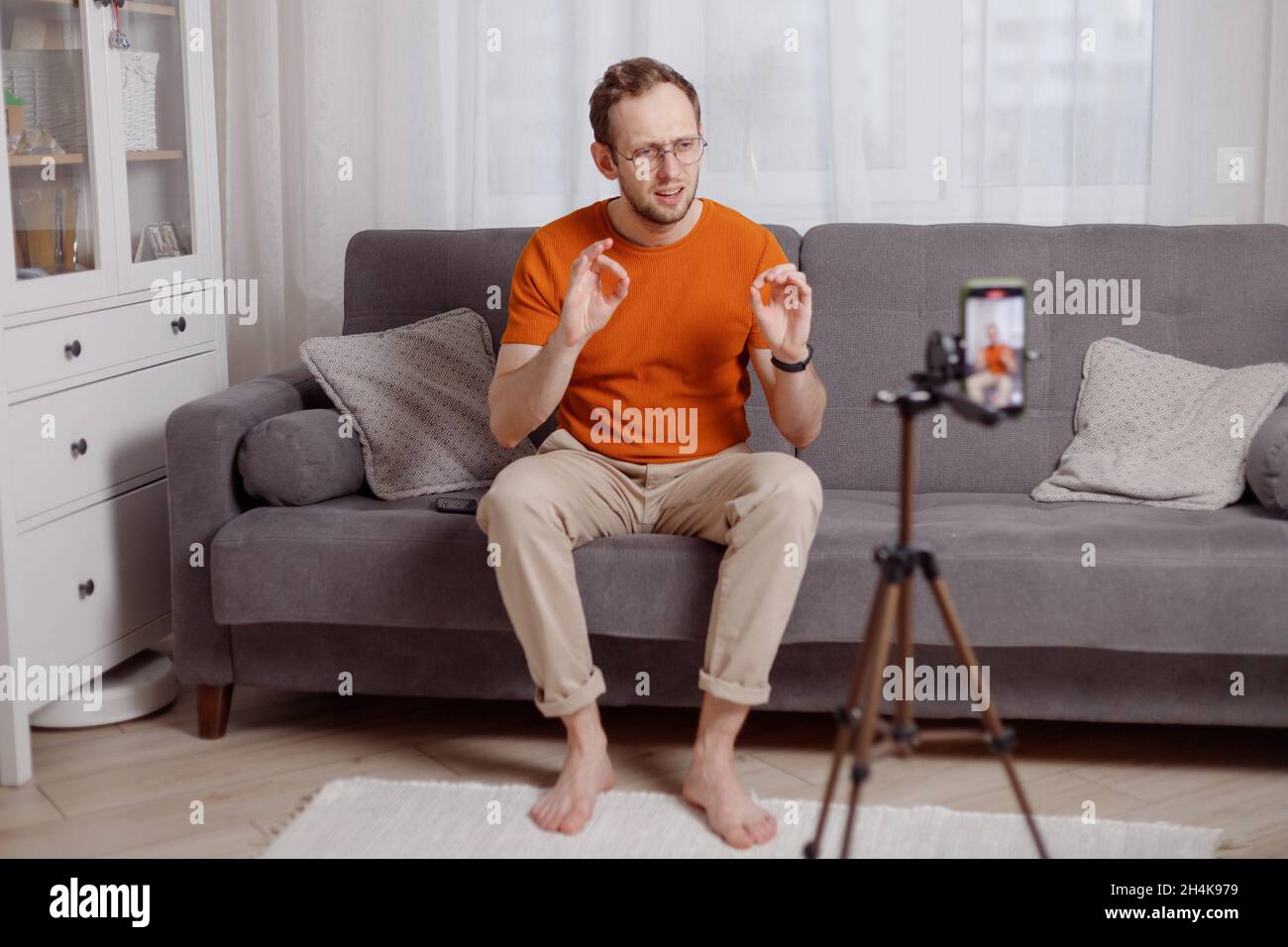 Hipster Mann Blogger Aufnahme Vlog auf Handy sitzen auf der Couch im Wohnzimmer und erklären und gestikulieren mit den Händen. Stockfoto
