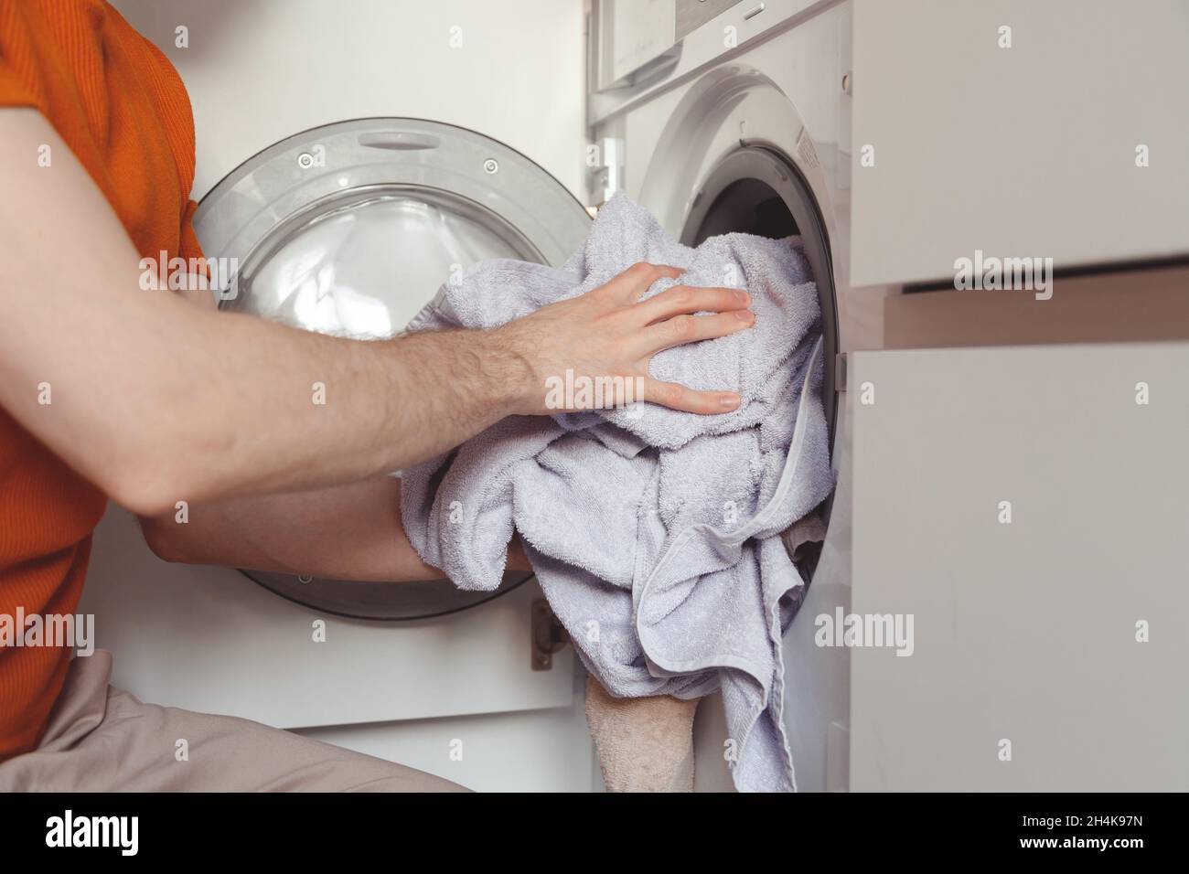 Mann, der farbige Kleidung und Handtücher in die eingebaute Waschmaschine einlädt. Stockfoto