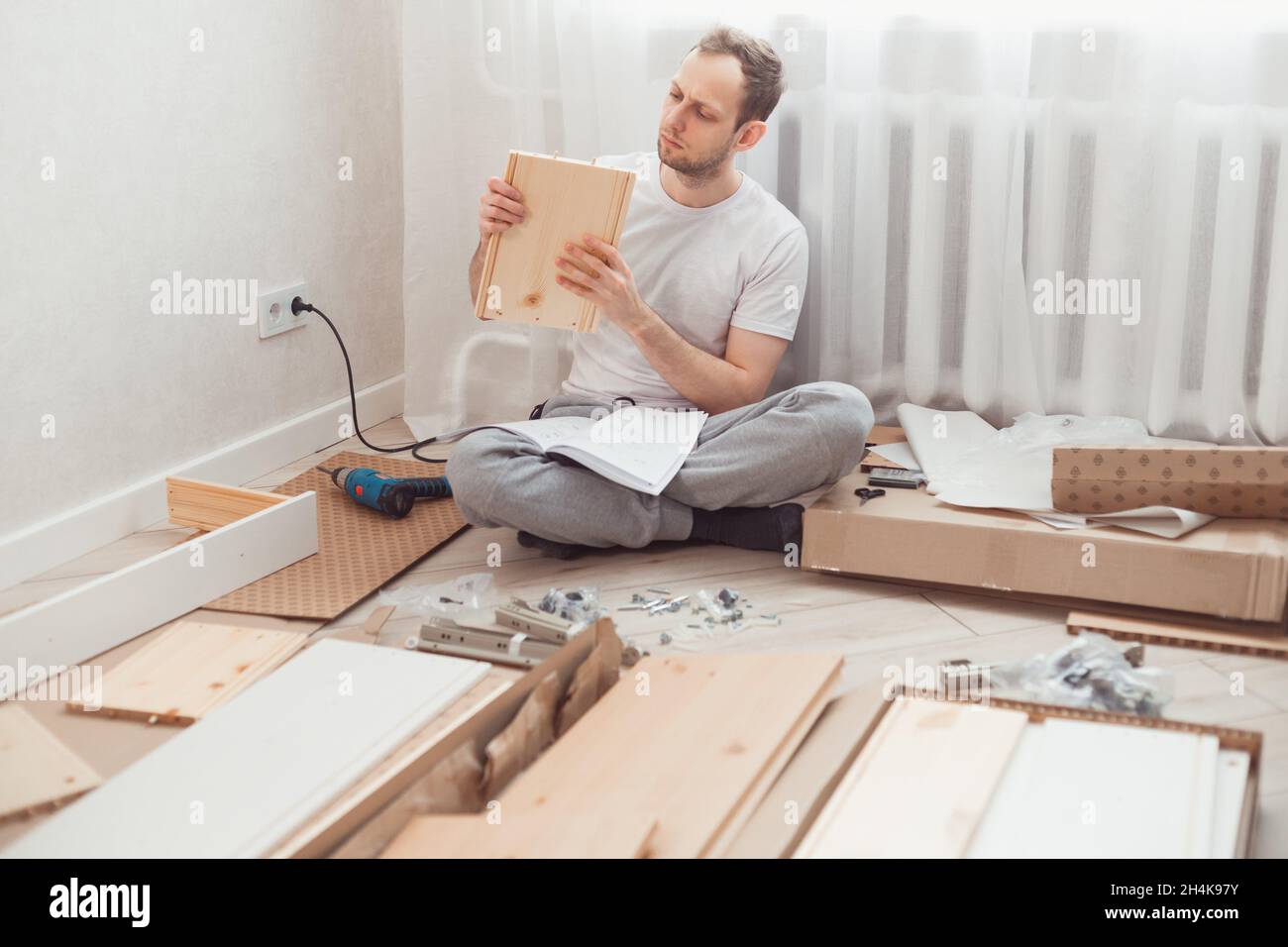Mann selbst Baugruppen Holzmöbel zu Hause ohne Meister. Lesen Sie die Anweisungen. Mann liest Anweisungen. DIY-Konzept. Stockfoto