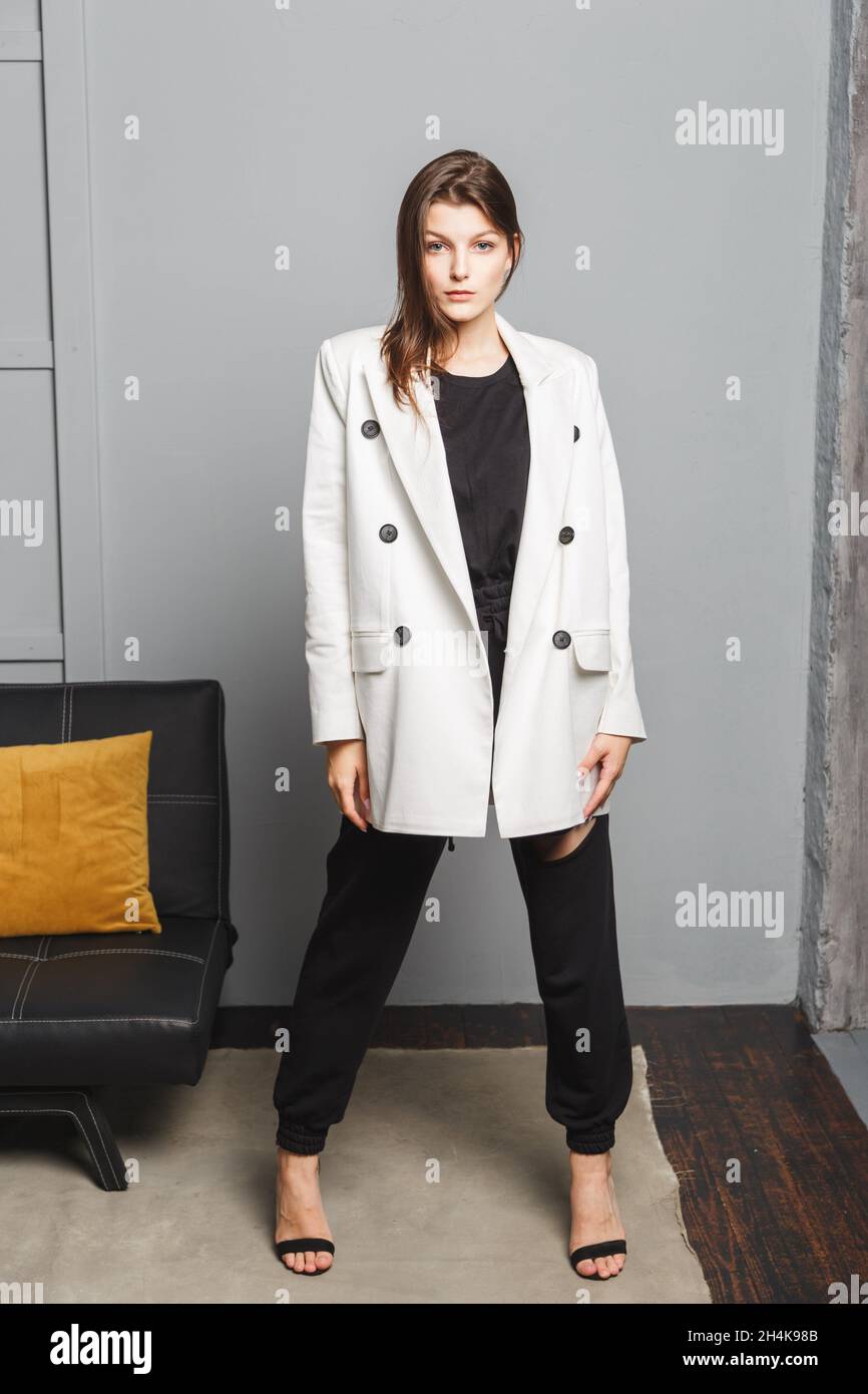 Junge elegante Frau in weißem Oversize-Blazer und schwarzen zerrissenen Hosen. Innenansicht im Hochformat. Stockfoto