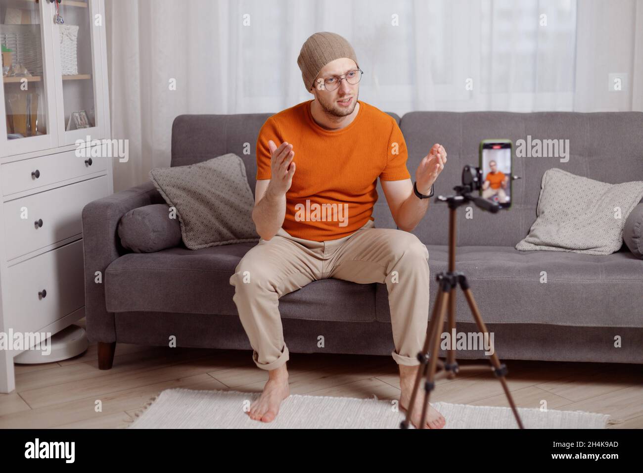 Millennial Hipster Mann Blogger Aufnahme vlog auf Handy sitzen auf dem Sofa im Wohnzimmer und erklären und gestikulieren mit den Händen. Inhalte für Stockfoto