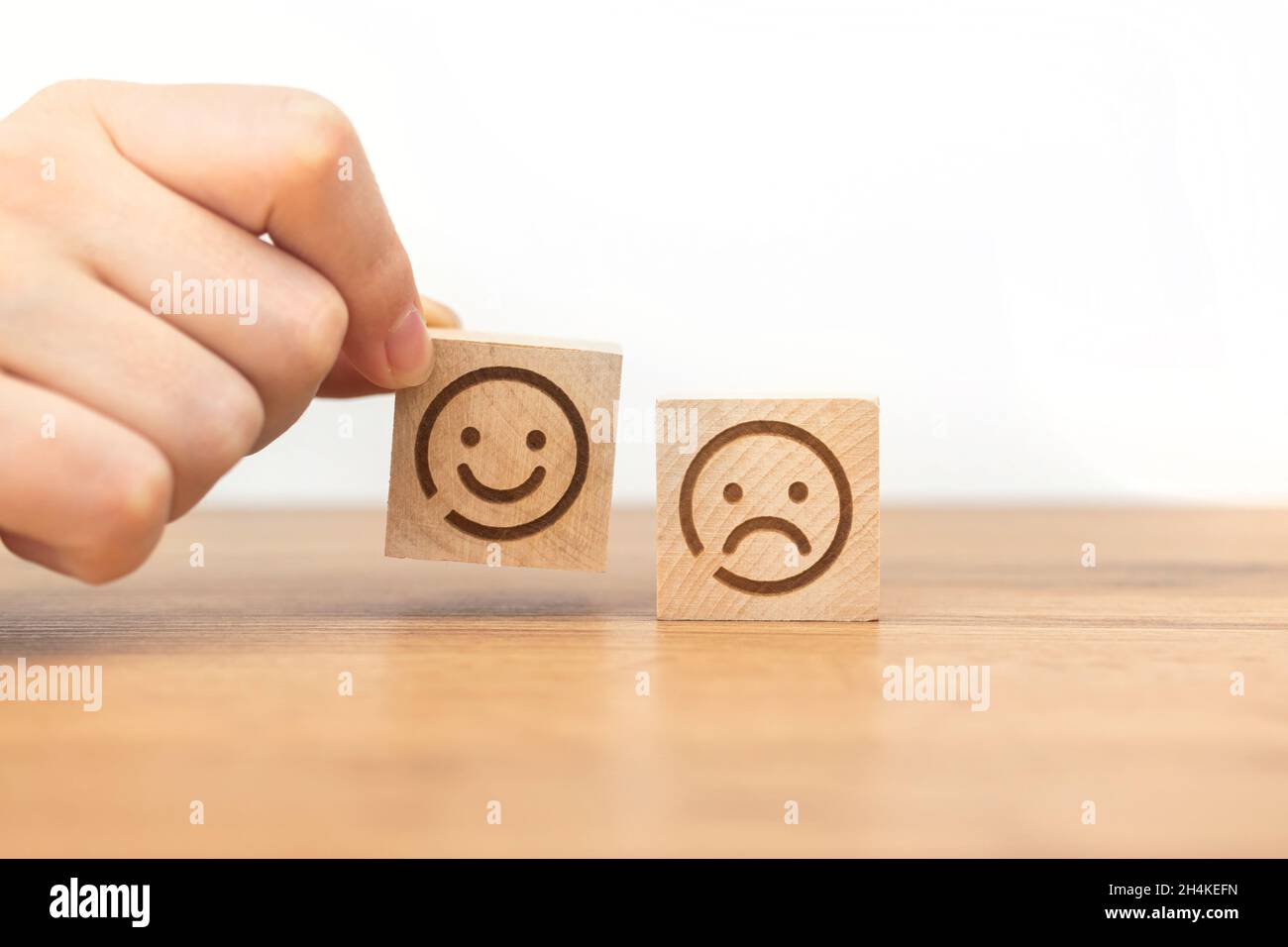 Die Hand des Kunden wählt das Smiley-Gesicht-Symbol auf einem Holzwürfel. Service-Rating, Zufriedenheit und Marketing-Konzept Stockfoto