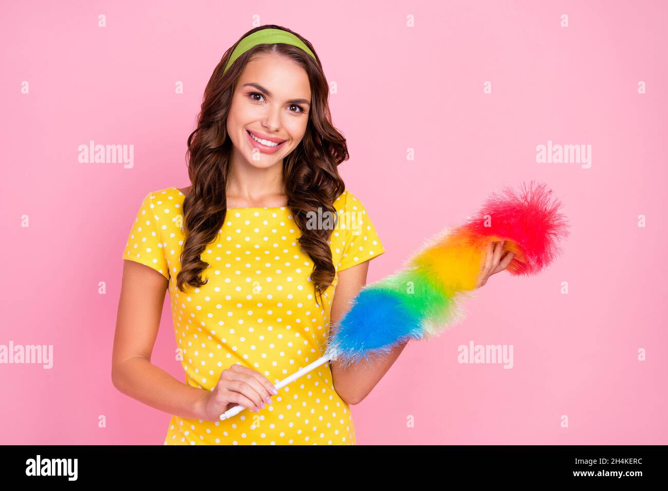 Foto von verträumten süßen jungen Dame gekleidet gepunkteten Kleid hält Staubwedel lächelnd isoliert rosa Farbe Hintergrund Stockfoto