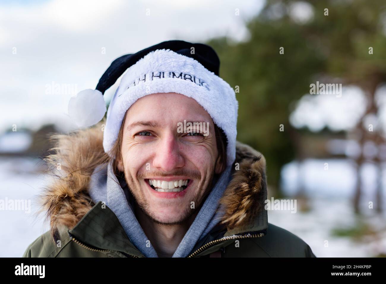 Ein ironisches Porträt eines lächelnden und glücklichen jungen Mannes, der einen schwarzen weihnachtsmann-Hut mit den Worten Bah Humbug trägt Stockfoto