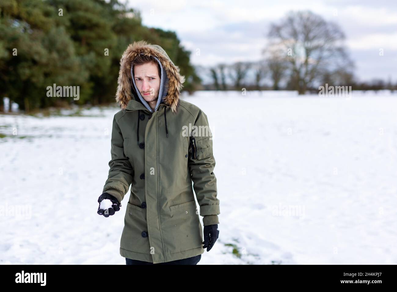 Ein entschlossen aussehender junger Mann mit einem Schneeball in der Hand, der bereit ist, ihn während einer Schneeballschlacht zu werfen. Er ist in einer schneebedeckten winterlichen Landschaft Stockfoto