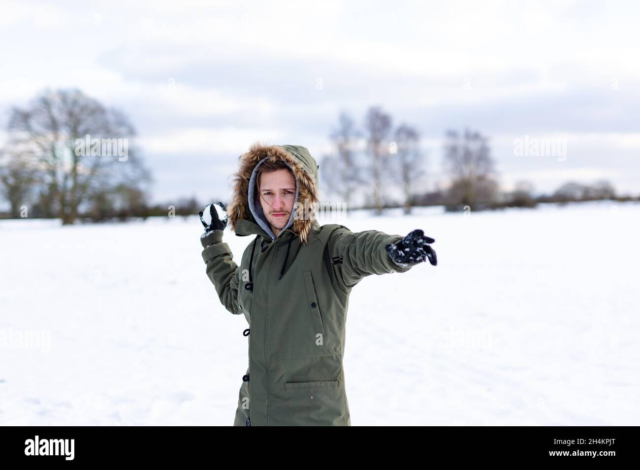 Ein entschlossen aussehender junger Mann mit einem Schneeball in der Hand, der bereit ist, ihn während einer Schneeballschlacht zu werfen. Er ist in einer schneebedeckten winterlichen Landschaft Stockfoto