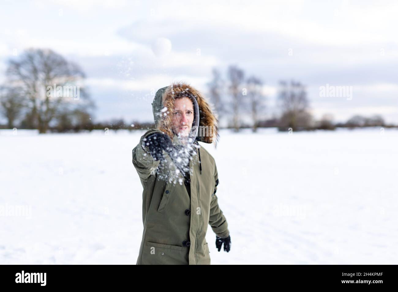 Ein entschlossener junger Mann, der einen Schneeball auf die Kamera wirft. Er ist in einer schneebedeckten winterlichen Landschaft Stockfoto