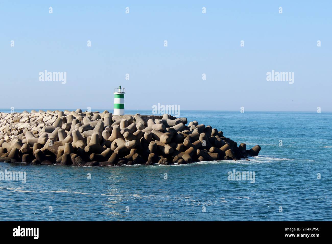 Der grün weiß gestreifen Leuchtturm auf dem Steg am Strand von Nazare. Portugiesische Bezeichnung: Farol Nazaré Pontão. Stockfoto