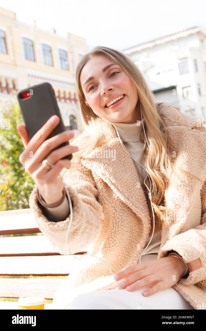 Vertikale Aufnahme einer fröhlichen Frau, die auf ihrem Smartphone Musik hört und Kopfhörer trägt Stockfoto