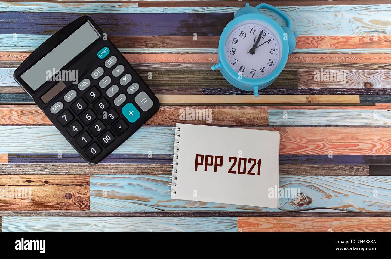 PPP 2021 auf einem Aufkleber, neben einem Rechner und einem Wecker auf einem Vintage-Hintergrund. Stockfoto