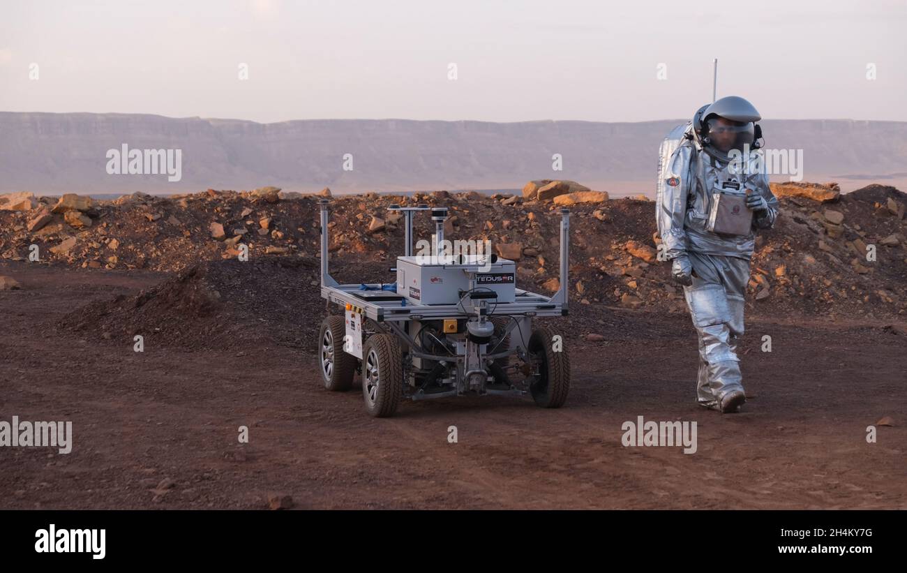 Ein analoger Astronaut, gekleidet in einen speziellen Raumanzügen, umläuft einen Rover auf dem Gelände der Mars-ähnlichen Forschungseinrichtung, die für die AMADEE-20-Mars-Simulation am Ramon-Krater in der Negev-Wüste in Israel gebaut wurde. Sechs Analogastronauten aus Israel, Portugal, Spanien, Deutschland, den Niederlanden und Österreich haben eine dreiwöchige Isolation innerhalb der Forschungseinrichtung abgeschlossen und konnten ihren Lebensraum nur in Raumanzügen verlassen. Das Team führte eine Reihe von wissenschaftlichen und technologischen Experimenten durch, in der Hoffnung, die Grundlagen für zukünftige bemannte Missionen zum Mars zu schaffen. Stockfoto