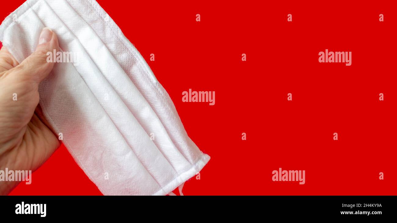 Eine weibliche Hand hält eine medizinische Maske auf einem roten Hintergrund. Atemschutzmaske. Nahaufnahme, Platz zum Kopieren, Draufsicht, flach liegend. Stockfoto