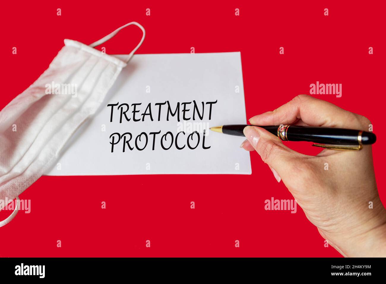 Das Wort Behandlungsprotokoll wird von einem Arzt auf einem roten Hintergrund in der Nähe einer medizinischen Schutzmaske geschrieben. Medizinisches Konzept Stockfoto