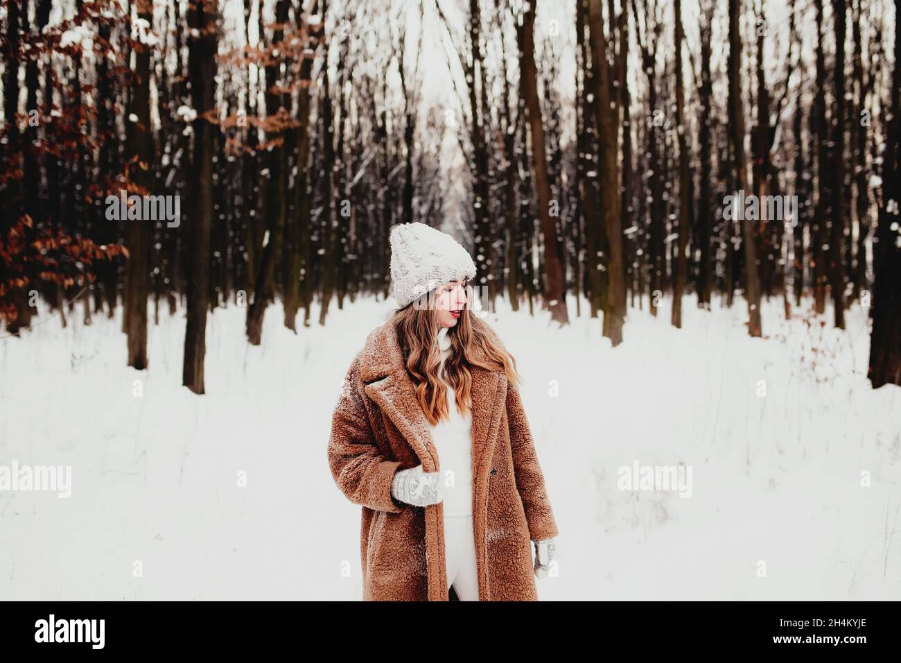 Foto einer jungen schönen Frau im Pelzmantel, die im Winterwald auf dem weißen Schnee steht. Mädchen lächelt und ist glücklich mit geschlossenen Augen. Weibchen hat Winter Stockfoto